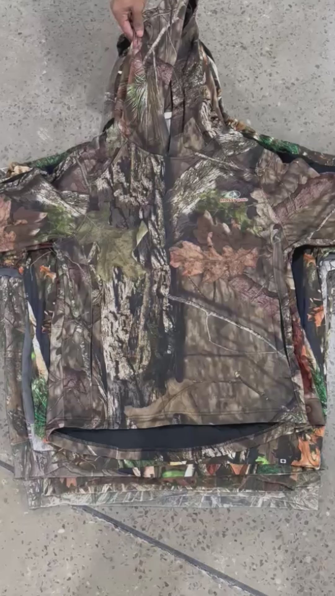 Collection of real tree style sweatshirts with camoflash prints  being pulled from a neatly stacked pile of sweatshirts in a gallery layout